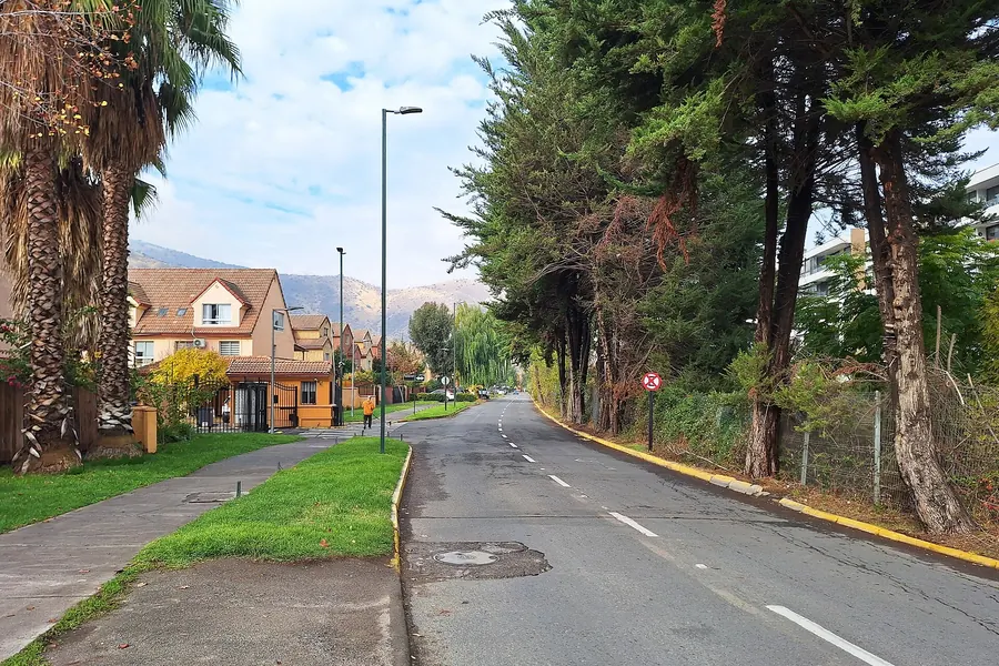 Calle residencial arbolada en Huechuraba, con casas de dos pisos y el cerro al fondo
