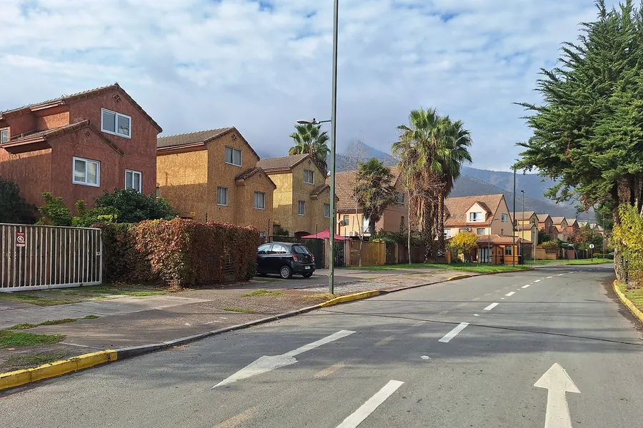 Casas de dos pisos en una avenida de Huechuraba, con palmeras y cerros al fondo